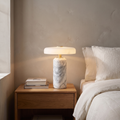 Ophira contemporary glass and marble LED table lamp glowing warm on a bedroom nightstand