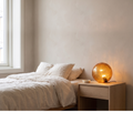 Oriane modern amber glass orb table lamp glowing warm on a bedroom nightstand