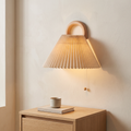 Modern solid beechwood semi-circle wall sconce with beige pleated fabric shade glowing above an oak nightstand