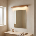 Japanese simple solid wood strip LED wall sconce glowing above a bathroom vanity mirror on a lime-washed plaster wall