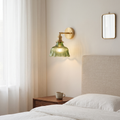 Nordic brass flower wall sconce with ribbed green glass shade glowing warm beside a linen headboard