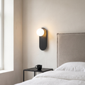 Nordic minimalist black pill-shaped glass globe wall sconce glowing warm beside a greige headboard