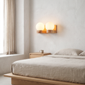Contemporary Nordic rubberwood 2-light glass globe wall sconce glowing warm above an oak nightstand beside a linen bed
