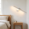 Nordic minimalist white aluminum long bar LED wall sconce glowing warm beside an oak bed above a nightstand