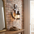 Industrial vintage white-washed wood boat anchor wall sconce with black iron glass lantern glowing on a brick hallway wall