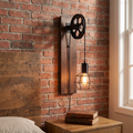 Vintage industrial pulley wall sconce with dark brown wood backboard and Edison cage lamp glowing on a brick wall beside a bed
