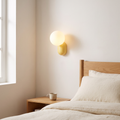 Macaron cream style yellow resin and frosted glass globe wall sconce glowing warm beside an oak bed in a Scandinavian bedroom