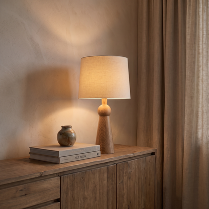 Velaris E27 table lamp lit at dusk on a wooden sideboard with art books and ceramic vase