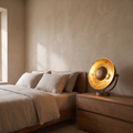 Castellane brass and iron table lamp glowing warm on a bedside chest in a refined modern bedroom