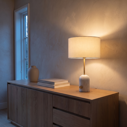Rivelle marble table lamp lit warm on a living room console at dusk