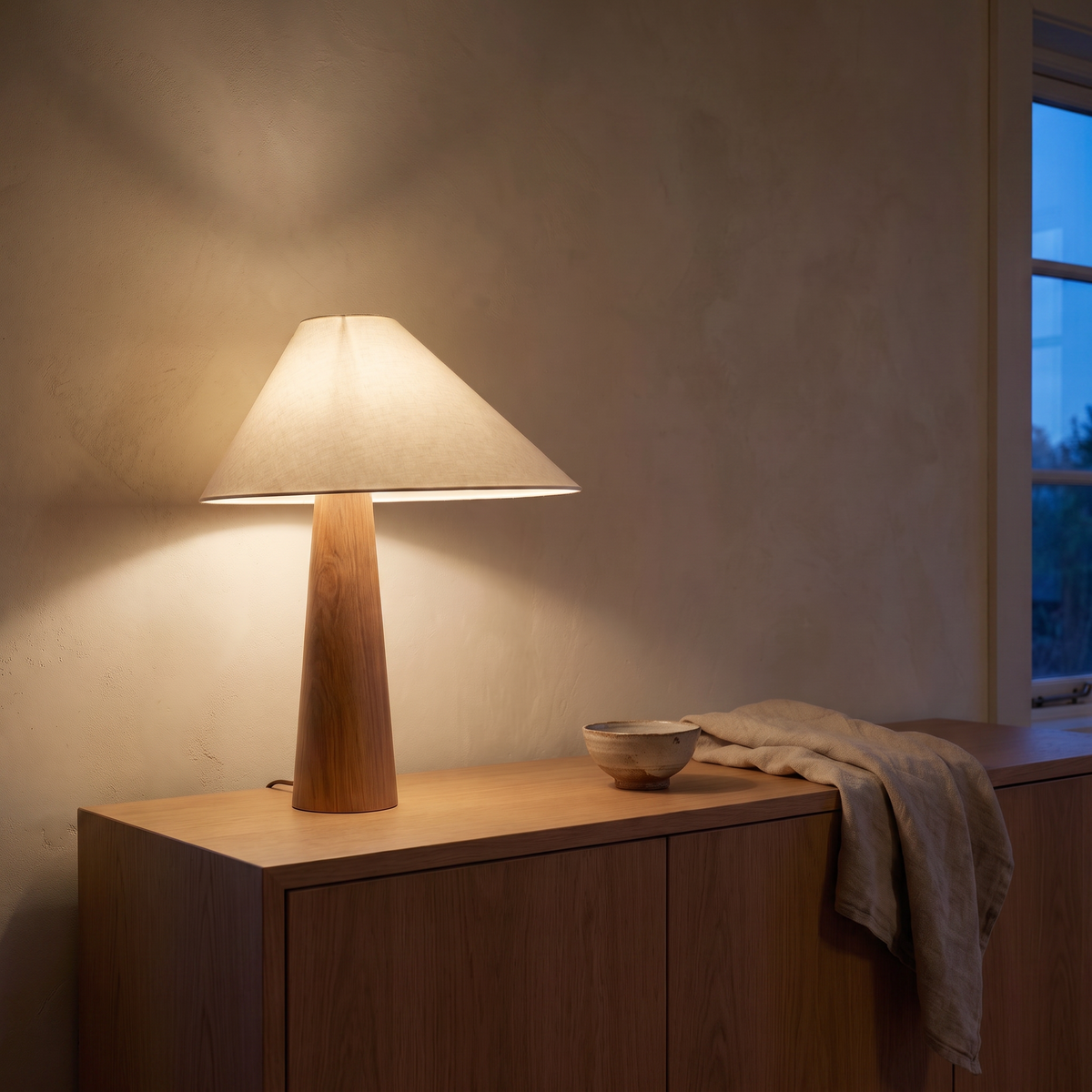 Verdoni fabric and wood lamp lit warm on an oak sideboard at dusk