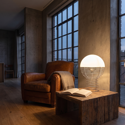Maravelle glass table lamp lit warm beside a leather armchair at dusk