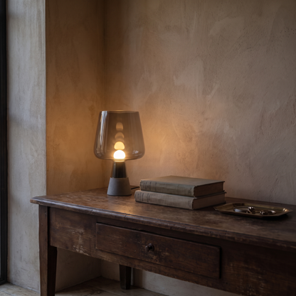Noctura small vintage glass lamp lit warm on a dark wood console at dusk