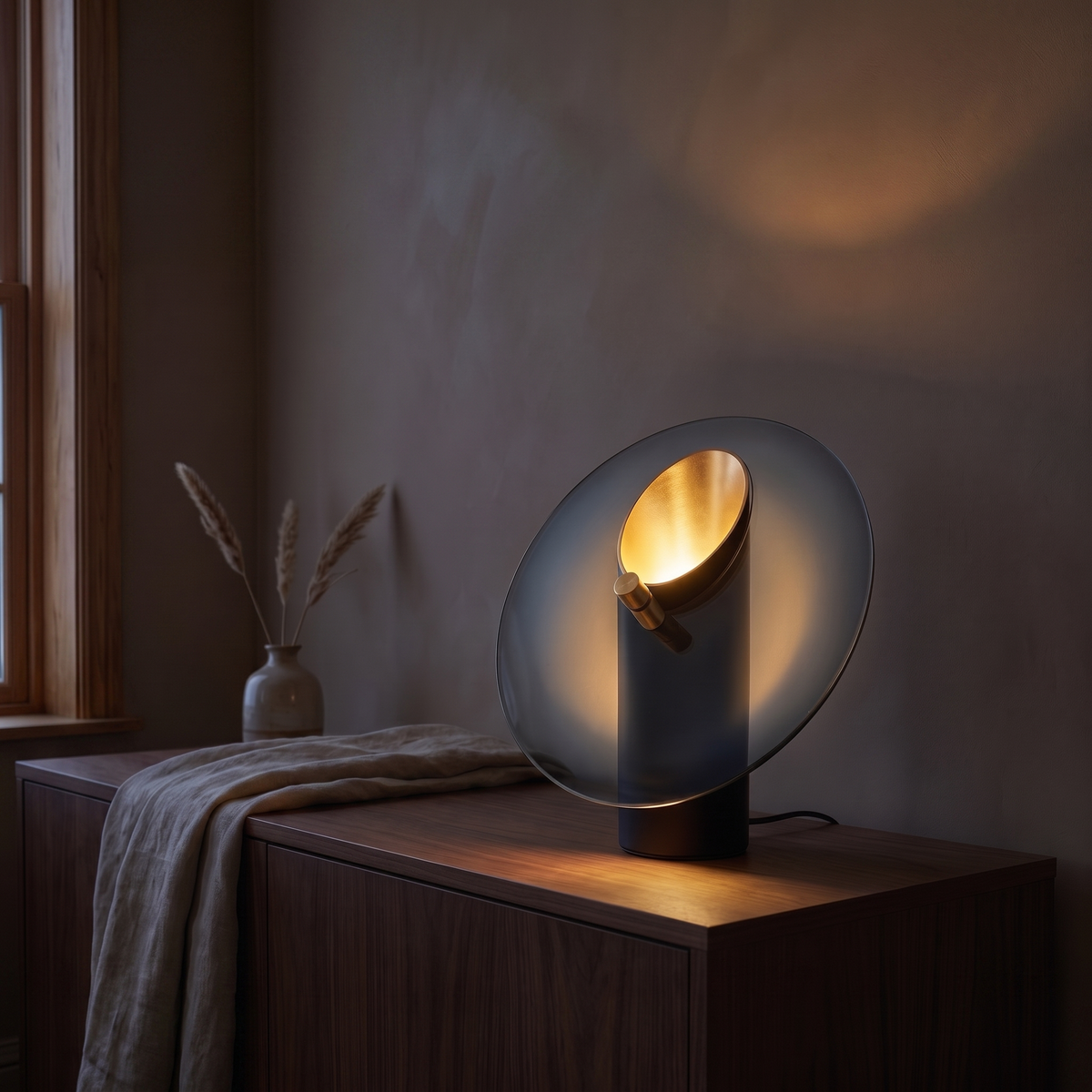 Amberlyn glass and metal table lamp lit at dusk on a walnut living room console