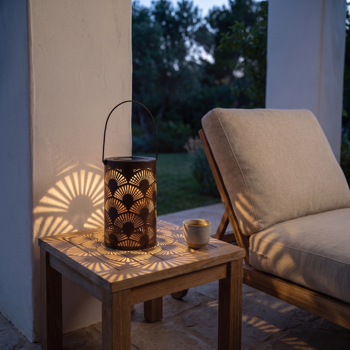Lucerna LED garden lantern casting patterned light on an evening patio side table