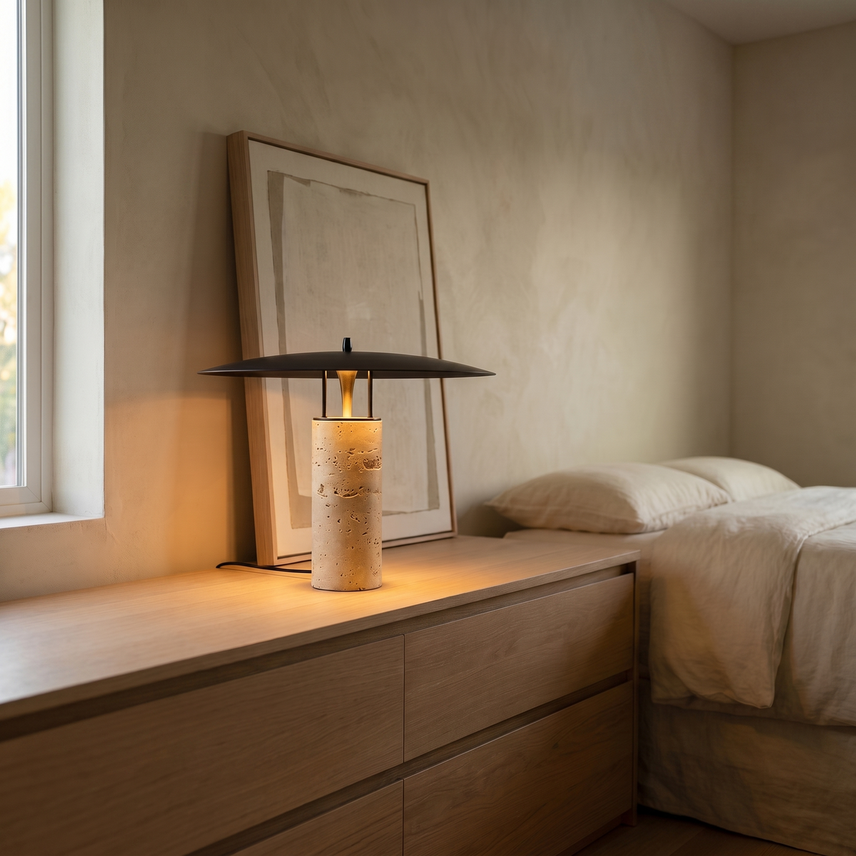 Marcheva modern travertine table lamp with black disc shade glowing on a bedroom dresser