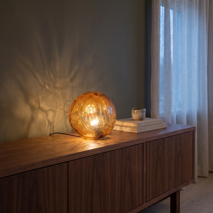 Oriane glass orb table lamp glowing on a walnut living room console at dusk