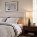 Cavour modern black marble table lamp with white drum shade lit beside an upholstered headboard