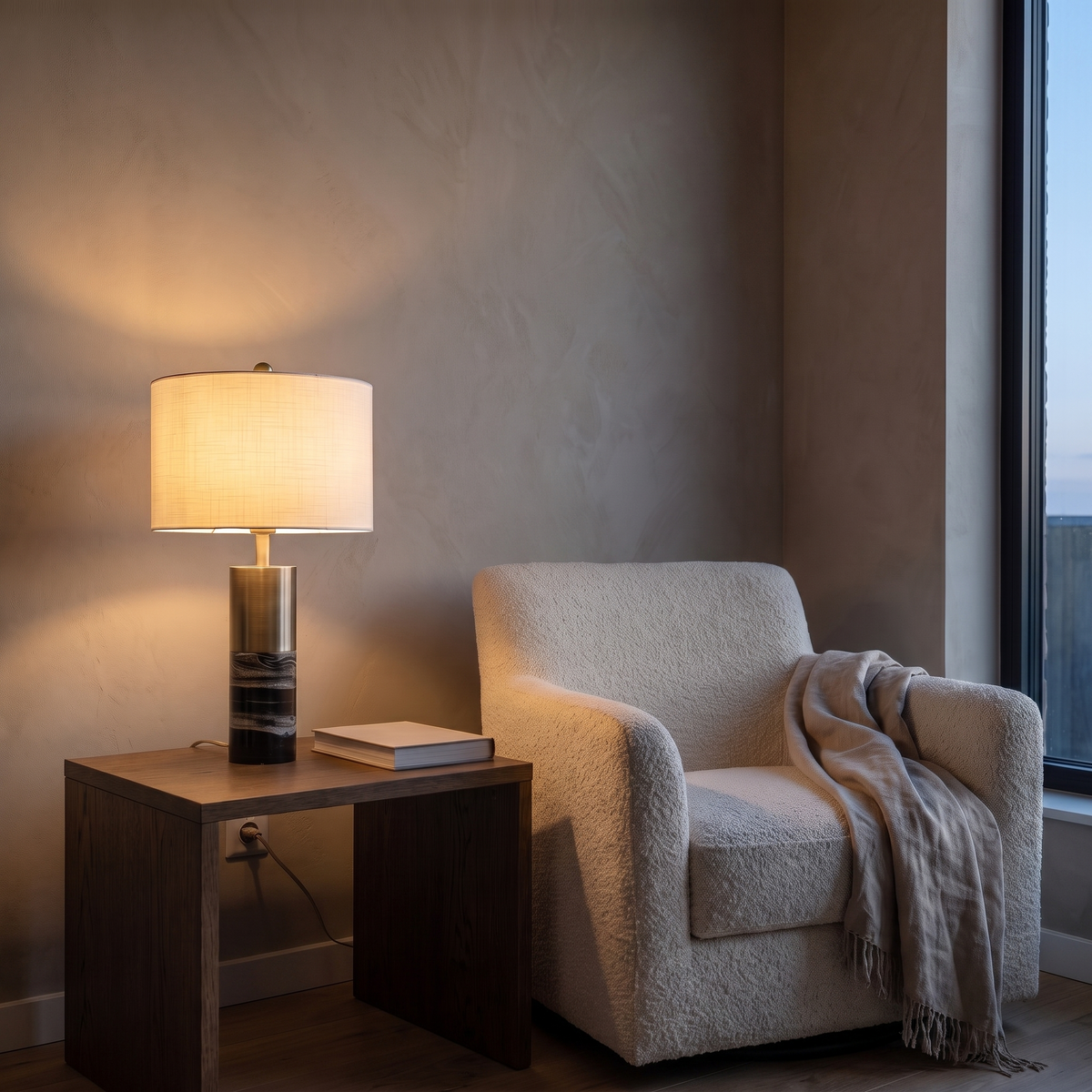 Cavour marble table lamp glowing warm beside a boucle armchair in a living room at dusk