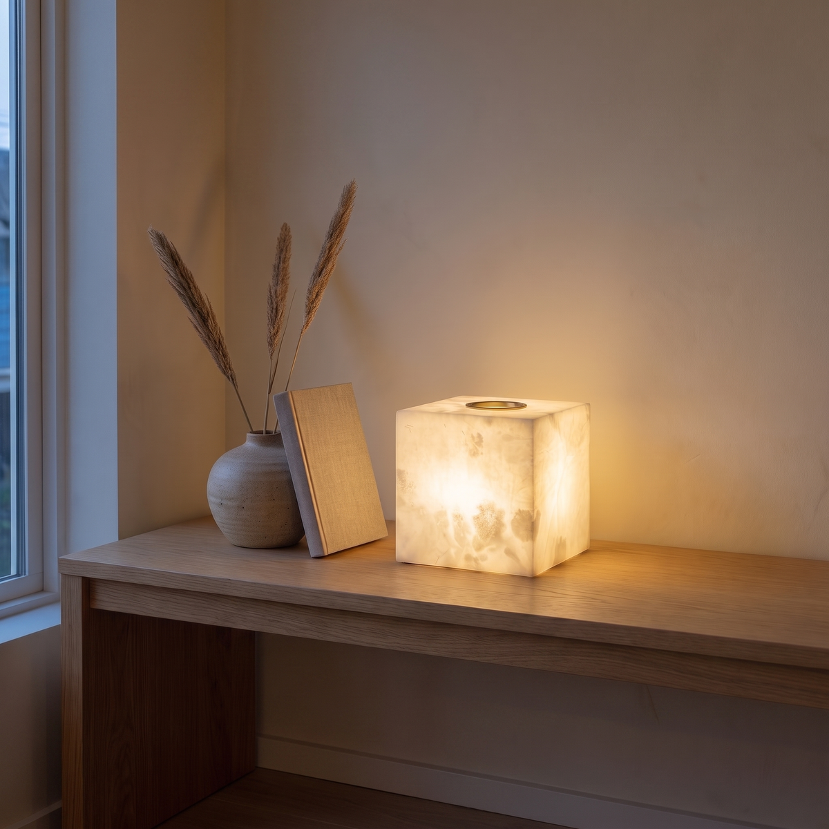 Duvessa alabaster cube lamp glowing from within on a light oak console at dusk