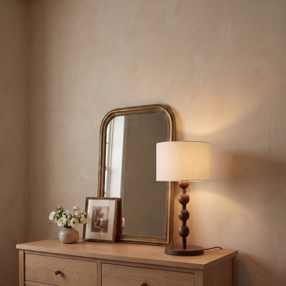 Montrave classic fabric and wood table lamp lit on a guest bedroom dresser with vintage mirror