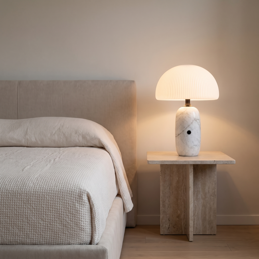 Opaline modern marble table lamp with frosted glass dome glowing on a travertine bedside table