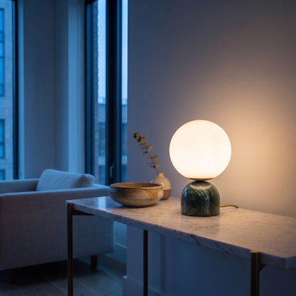 Willowmere marble and brass table lamp lit warm on a living room console at dusk