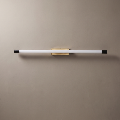 Thin aluminum PC tube LED wall sconce with gold center mount and black end caps on a greige plaster wall, lamp off