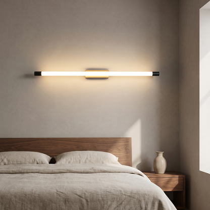 Modern minimalist thin tube LED wall sconce in black and gold glowing warm above a walnut bed headboard