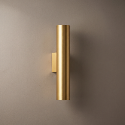 Gold brushed aluminum cylinder up-down LED wall sconce mounted on a plain greige plaster wall, lamp off