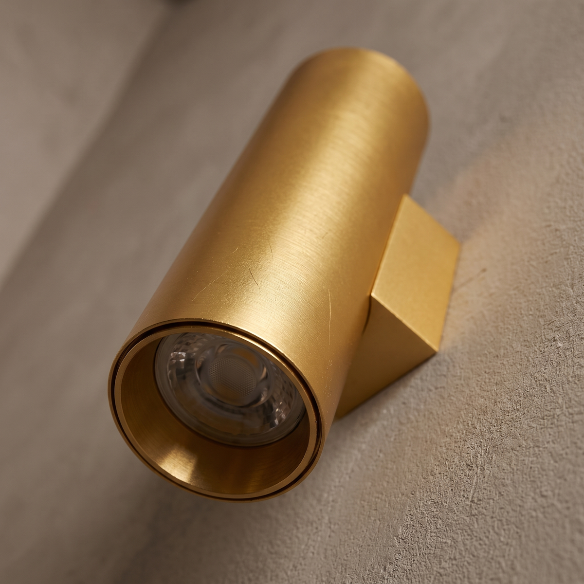 Close-up detail of the brushed gold aluminum cylinder wall sconce open end, LED lens and mounting bracket
