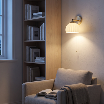 White striped glass brass 1-light wall sconce lit in a Nordic reading corner beside a bookshelf and linen armchair
