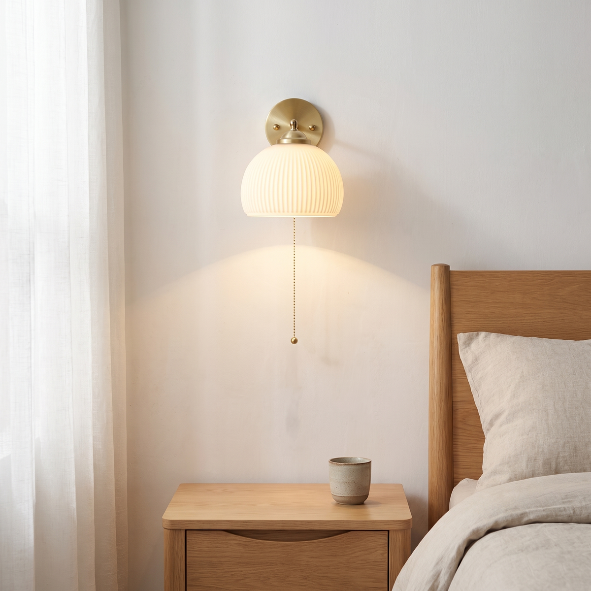 Nordic striped white glass brass pull cord wall sconce glowing warm beside a light oak bed and nightstand