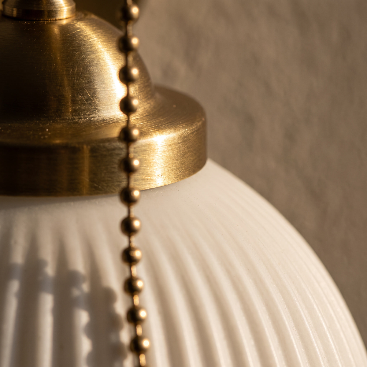 Close-up of the fluted white glass shade, brass collar and pull chain of the Nordic brass wall sconce