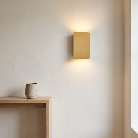 Nordic minimalist brushed gold aluminum rectangular flat panel LED wall sconce glowing up and down on a white plaster hallway wall