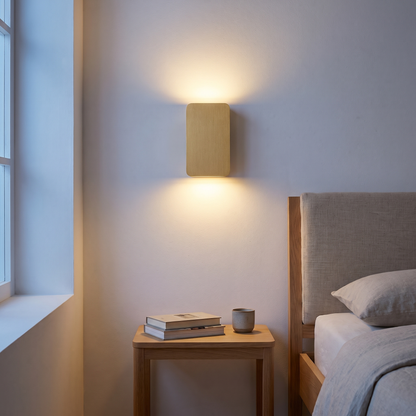 Gold rectangular up-down LED wall sconce lit beside an oak bed and nightstand in a Nordic bedroom at dusk
