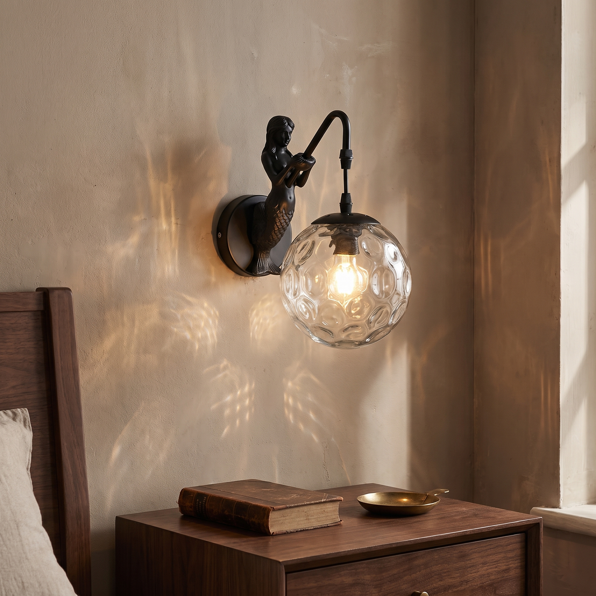 Vintage rustic black mermaid wall sconce with clear hammered glass orb glowing warm beside a walnut nightstand