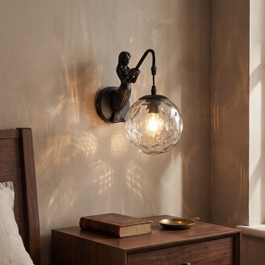 Vintage rustic black mermaid wall sconce with clear hammered glass orb glowing warm beside a walnut nightstand