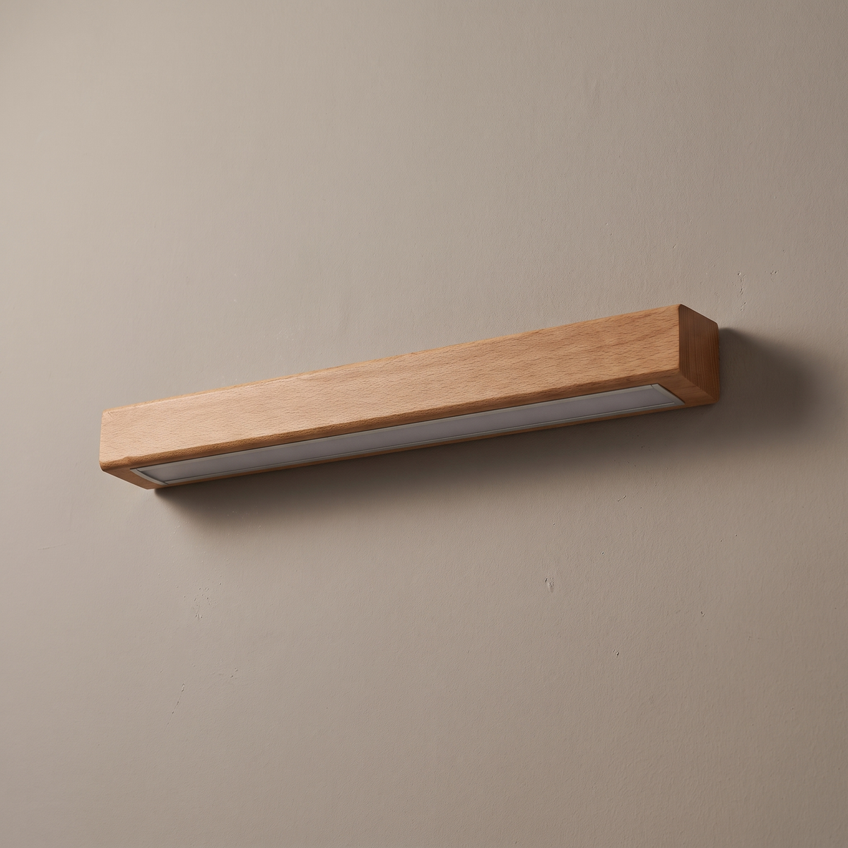 Brown solid wood linear LED wall light bar mounted on a greige plaster wall, lamp off