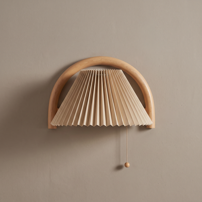 Solid wood semi-circle arch wall sconce with beige pleated shade and pull cord mounted on a greige plaster wall, lamp off
