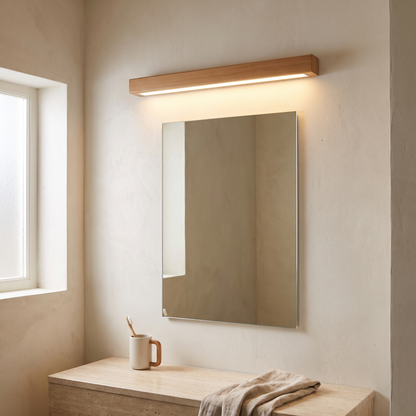 Japanese simple solid wood strip LED wall sconce glowing above a bathroom vanity mirror on a lime-washed plaster wall