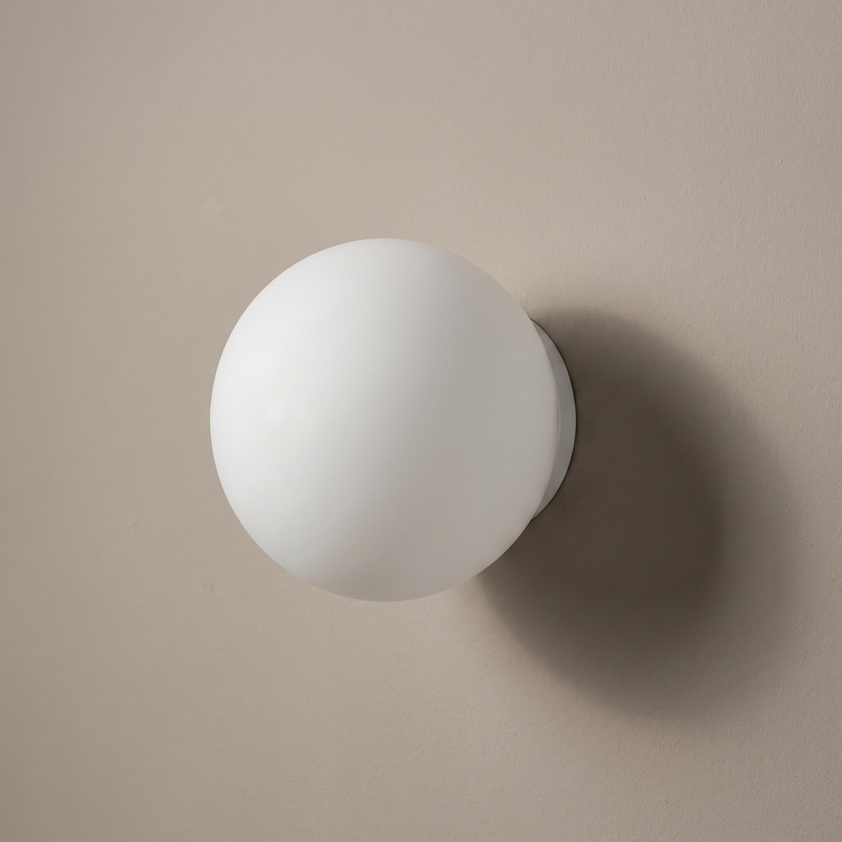 White frosted glass sphere 1-light wall sconce mounted on a greige plaster wall, lamp off
