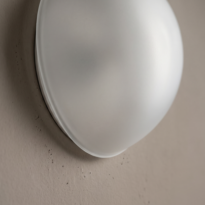 Close-up of the satin white opal glass orb shade meeting the plaster wall on the minimalist wall sconce