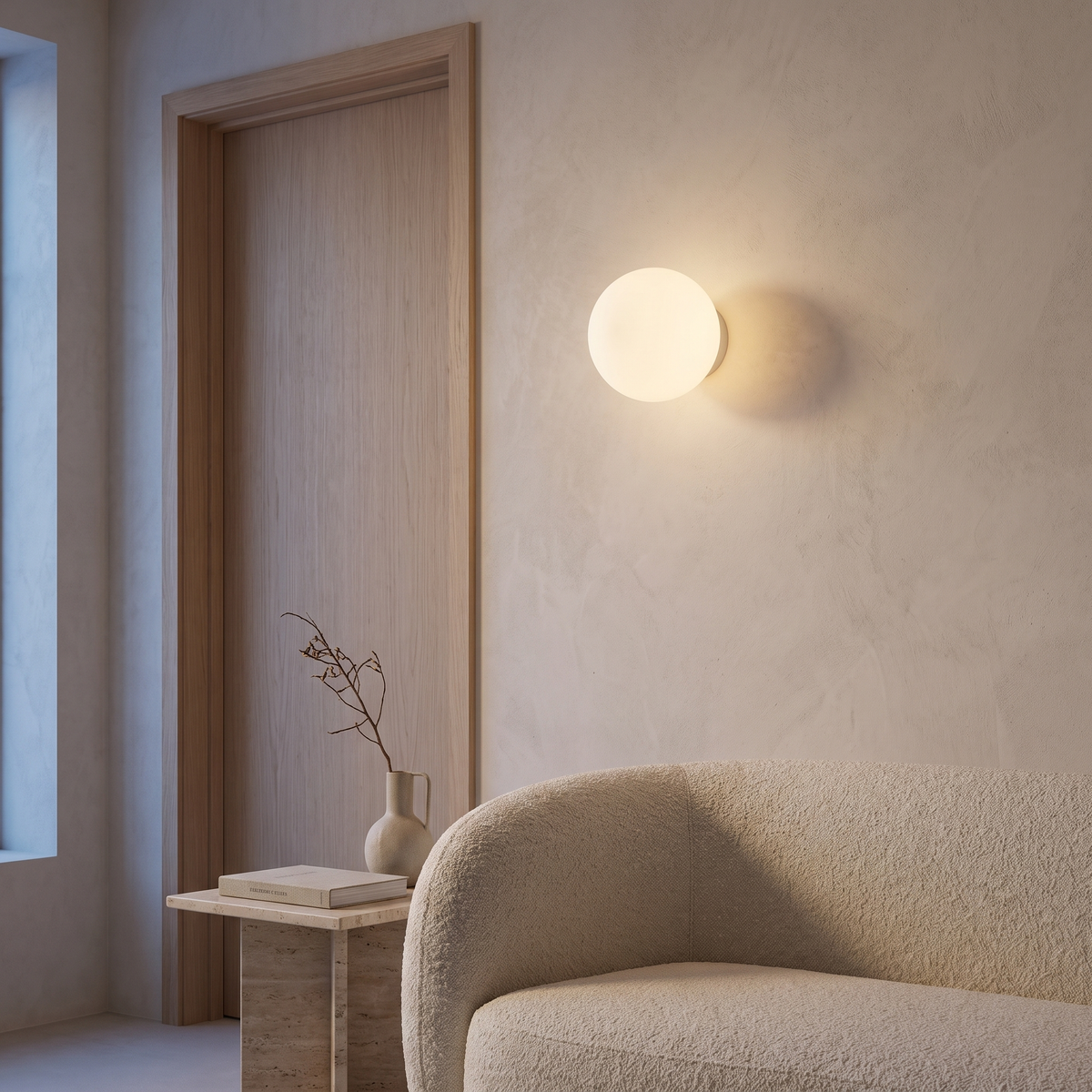 Opal glass orb wall sconce lit beside a pale oak door frame and boucle sofa in a warm minimalist living room at dusk
