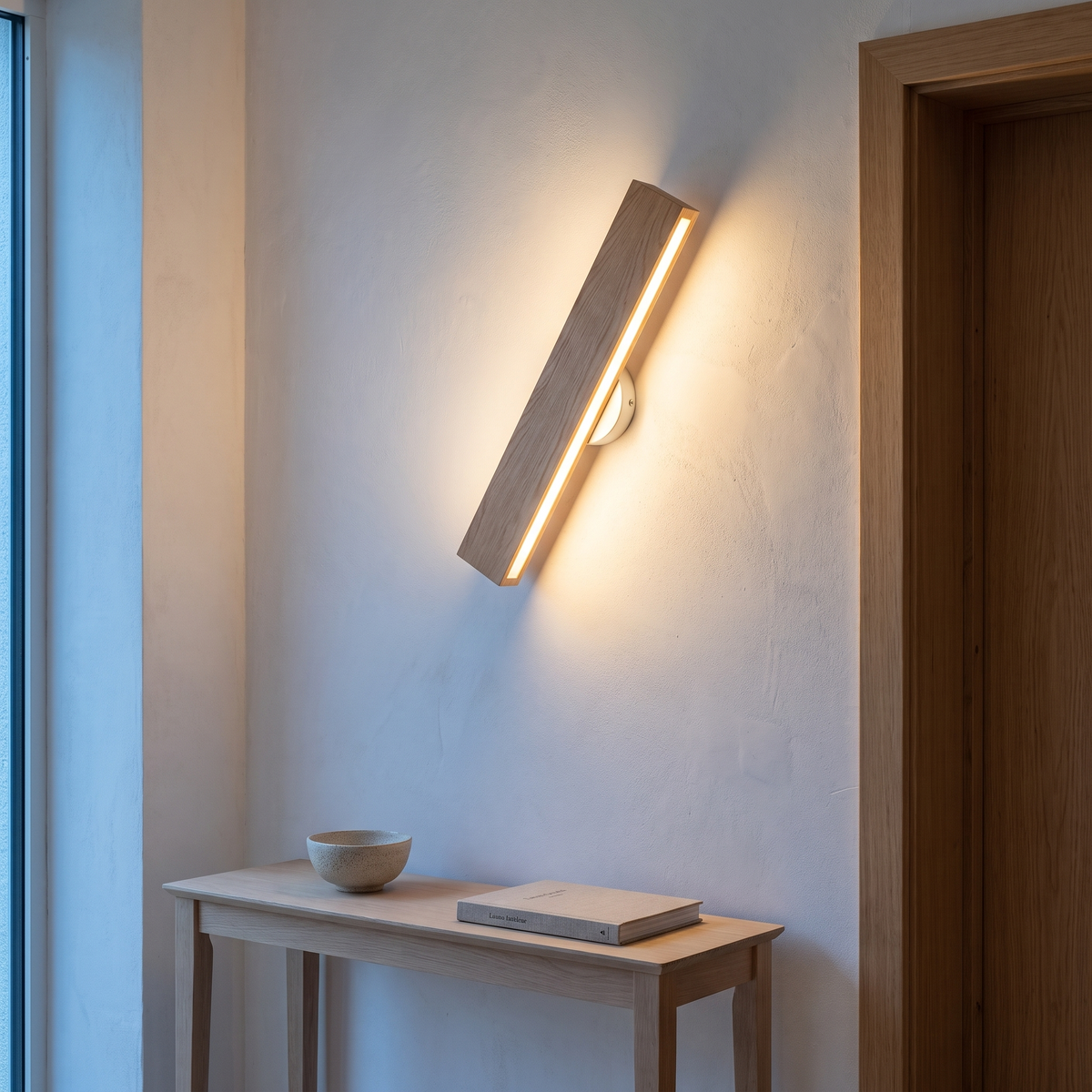 Nordic rotatable solid oak LED bar wall sconce rotated diagonally and lit at dusk above an oak console in a hallway beside a door frame