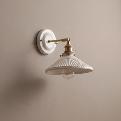 Vintage round ceramic backplate wall sconce with brass arm and white conical ceramic shade on a plain greige wall, lamp off