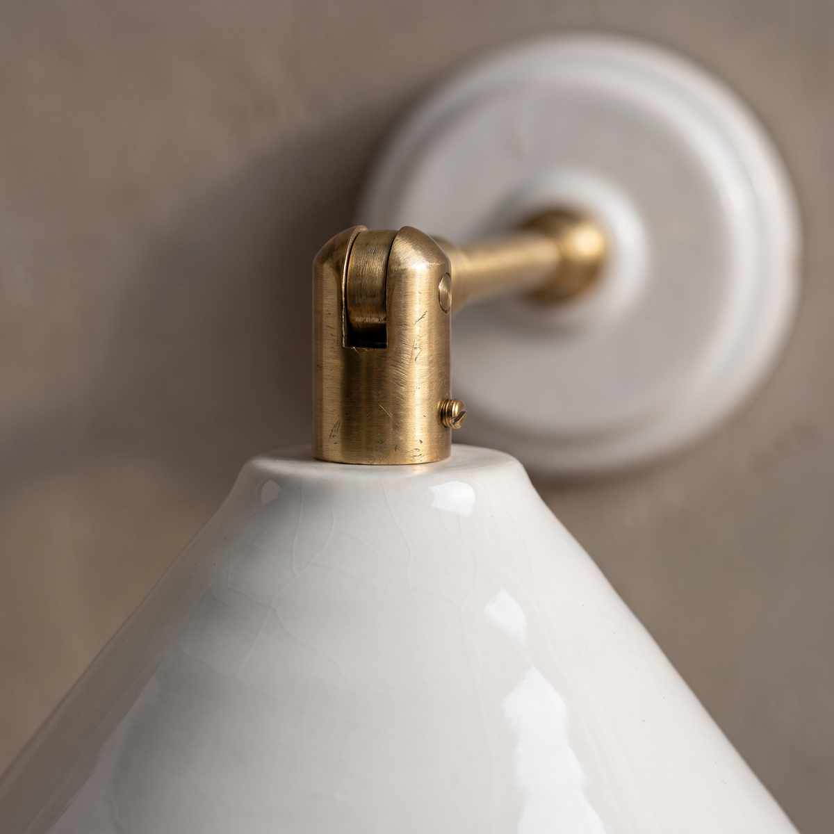 Close-up of the brass arm joint and glazed white ceramic shade of the traditional vintage wall sconce