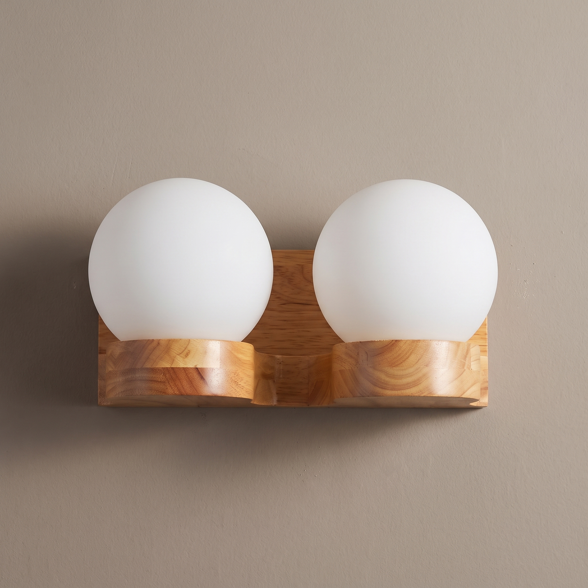 Nordic rubberwood 2-light wall sconce with two white opal glass globes on a plain greige plaster wall, lights off
