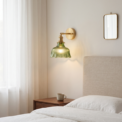Nordic brass flower wall sconce with ribbed green glass shade glowing warm beside a linen headboard