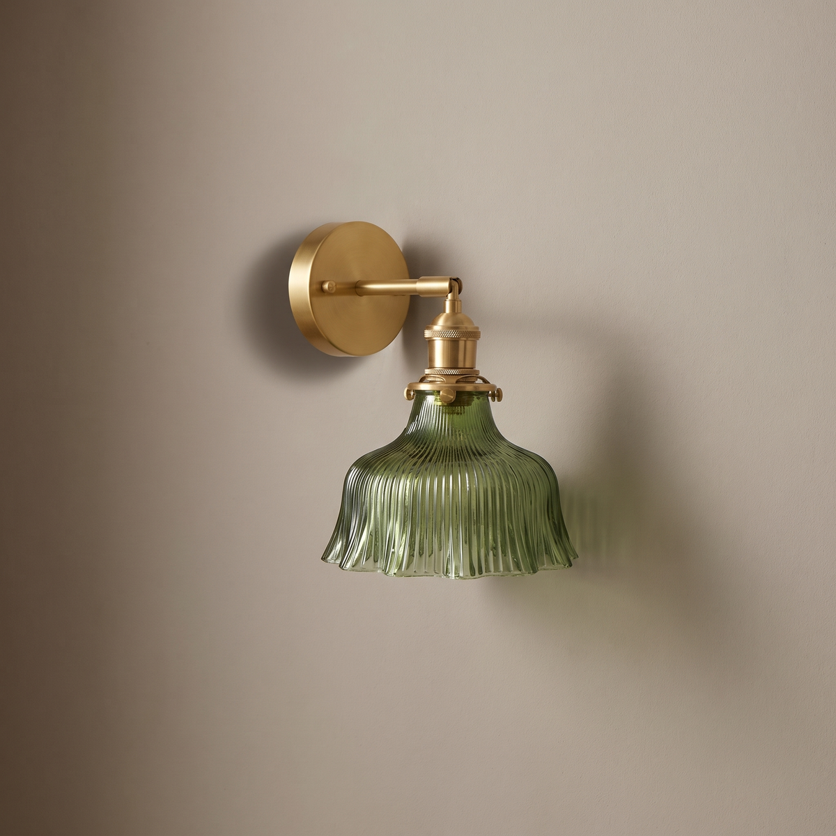 Brass copper 1-light wall sconce with green ribbed flower glass shade on a plain greige wall, light off